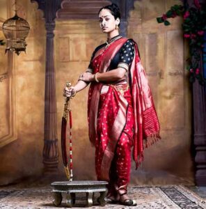 A woman dressed in traditional Nauvari saree poses with a sword, reflecting the martial legacy of Maratha women who wore the saree for ease during warfare and horseback riding.